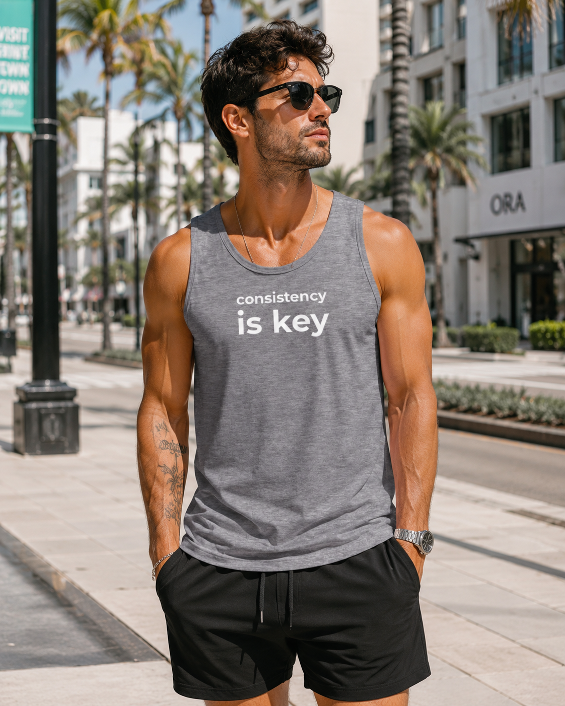 Man wearing a gray tank top with 'consistency is key' text on a city street.