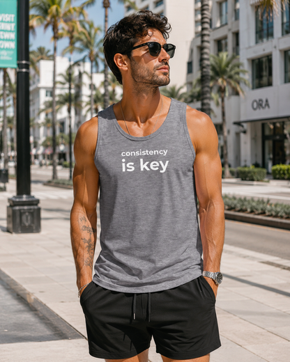Man wearing a gray tank top with 'consistency is key' text on a city street.