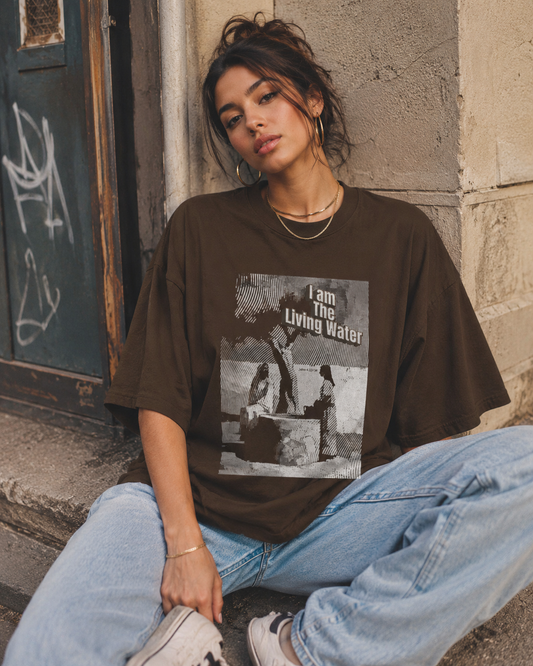 Person wearing a brown t-shirt with graphic design sitting against a wall.