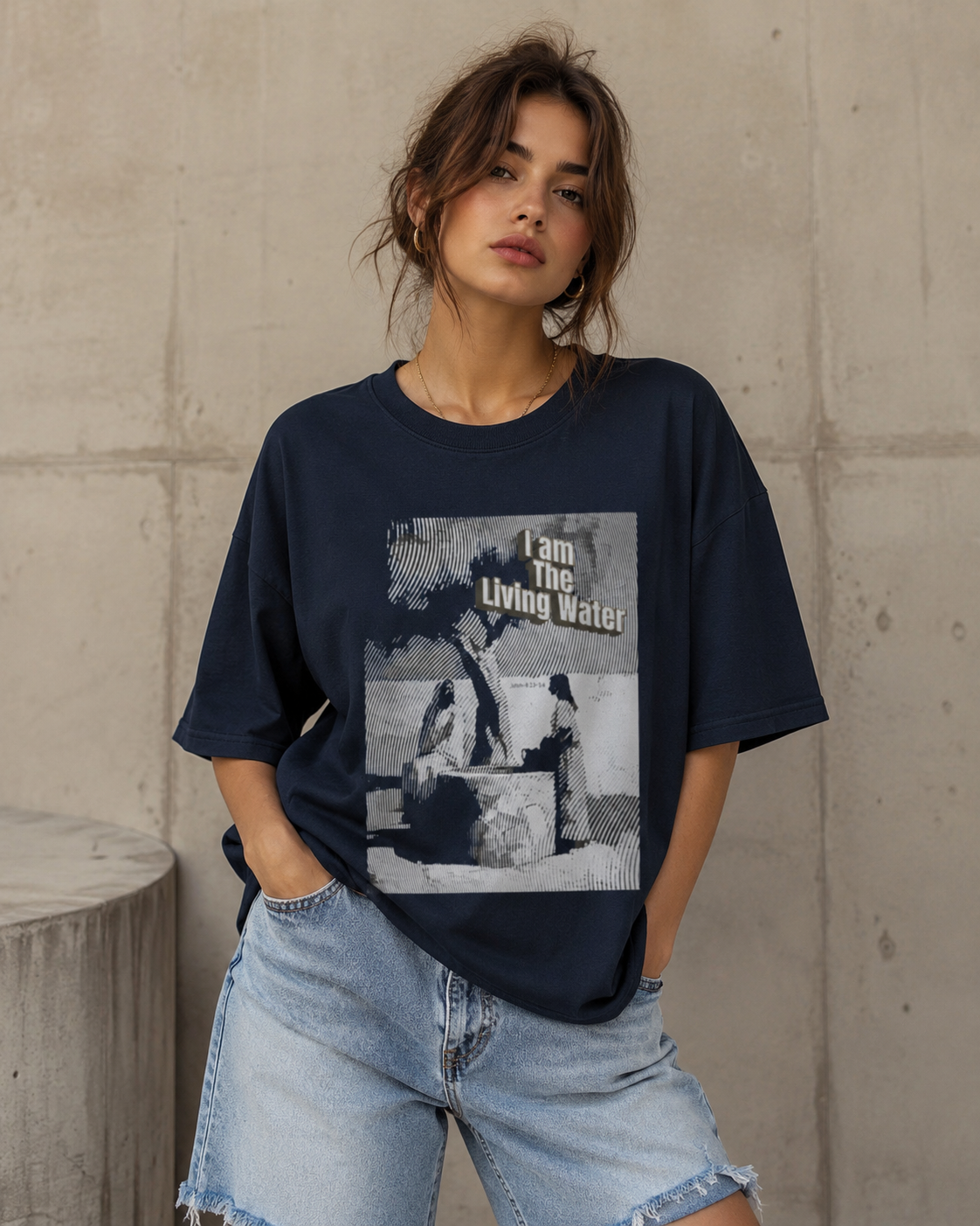 Person wearing a navy blue t-shirt with graphic design and text, standing against a concrete wall.